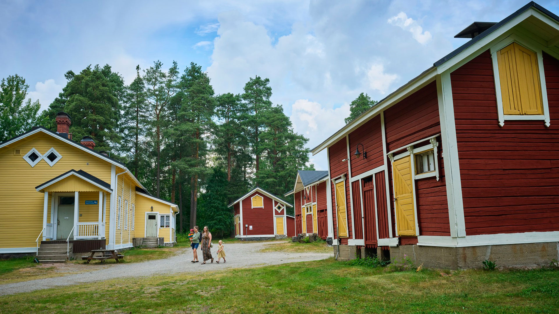 Pihapiirissä perinteisiä rakennuksia, joiden välissä kävelee kaksi naista, joilla mukanaan kaksi pientä lasta.