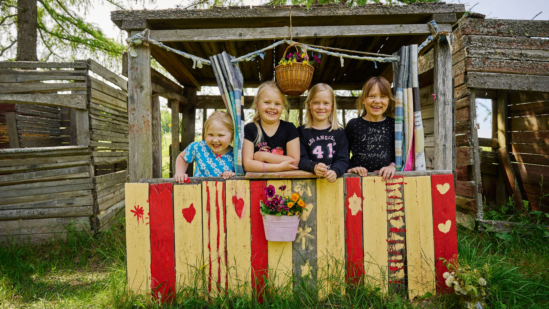 Neljä pientä tyttöä seisoo majarakennelmassa ja hymyilee.