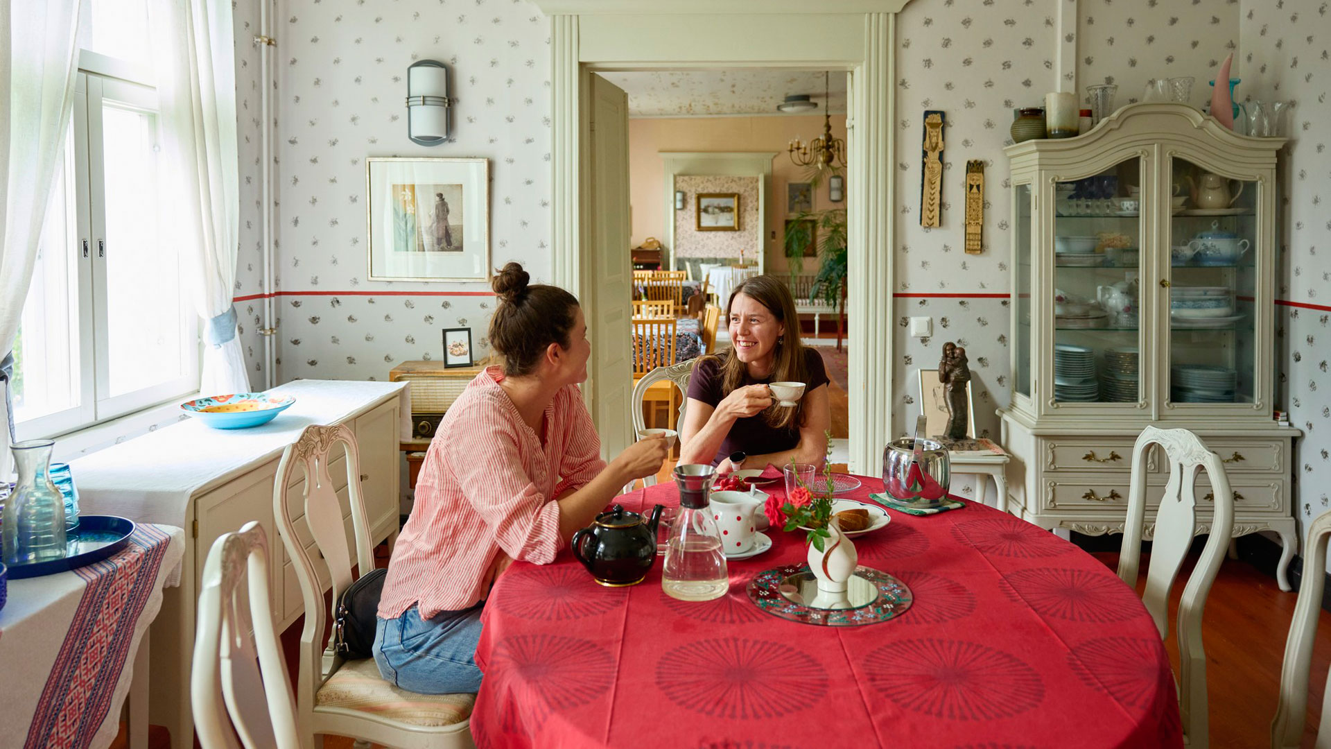 Kaksi naista istuu pöydän ääressä kahvikupit kädessään.