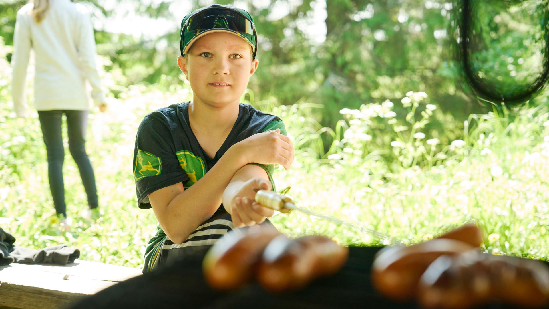 Poika istuu ja pitää makkaratikkua, jossa makkara paistumassa.